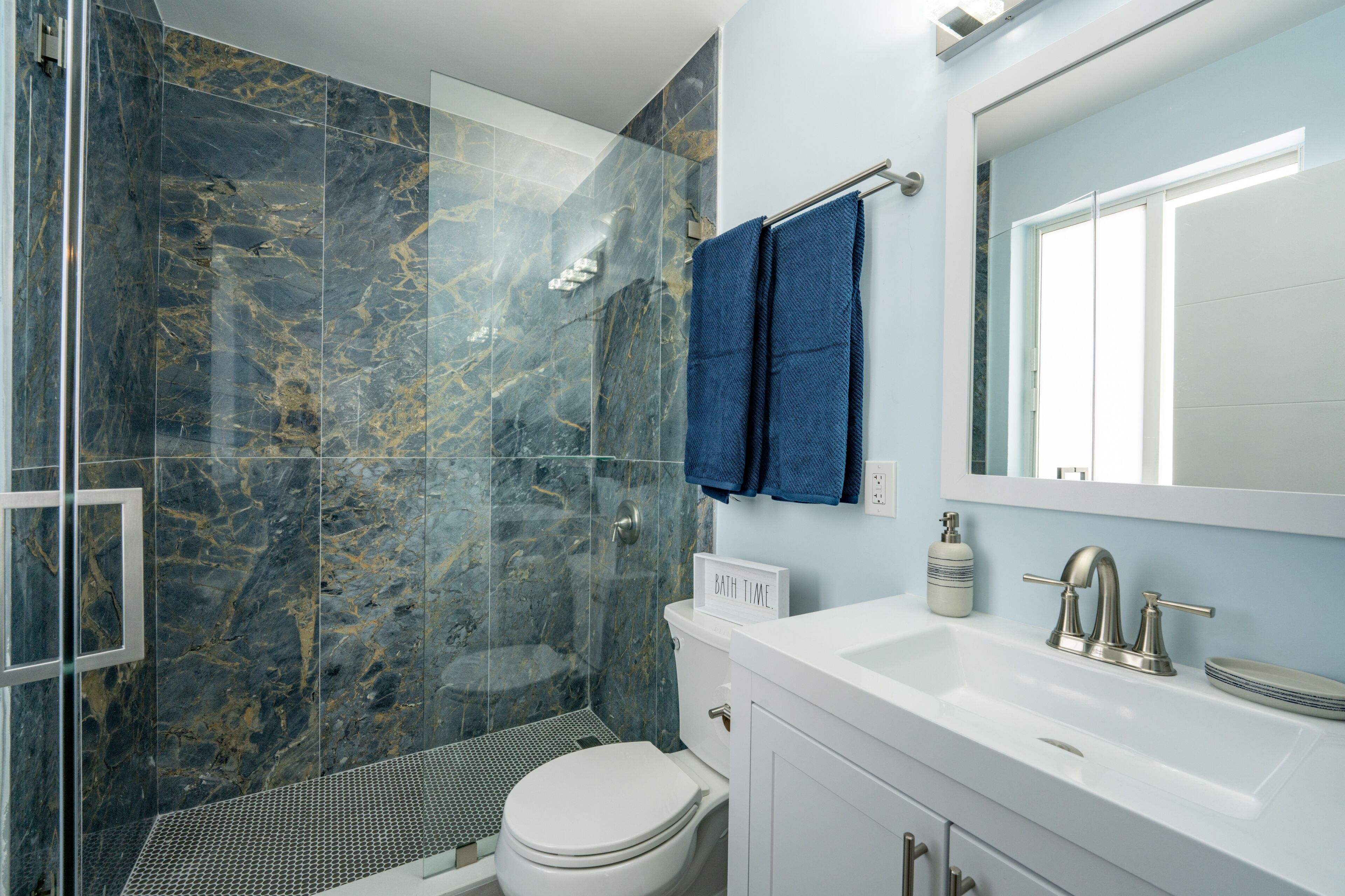 A modern bathroom with a glass-enclosed shower, a white toilet, and a sink with a mirror above it.