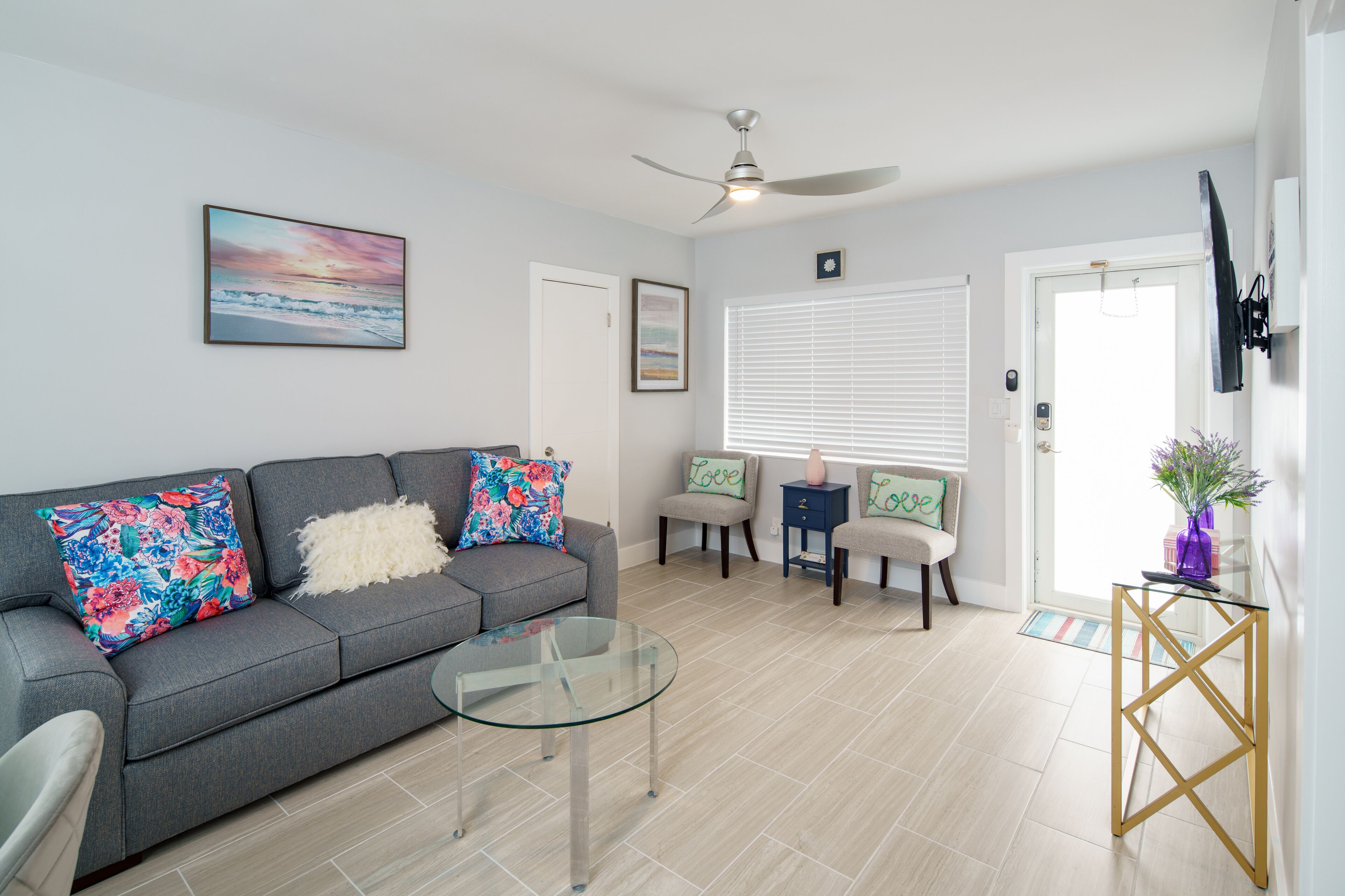 A modern living room with a grey sofa, glass coffee table, and a ceiling fan.