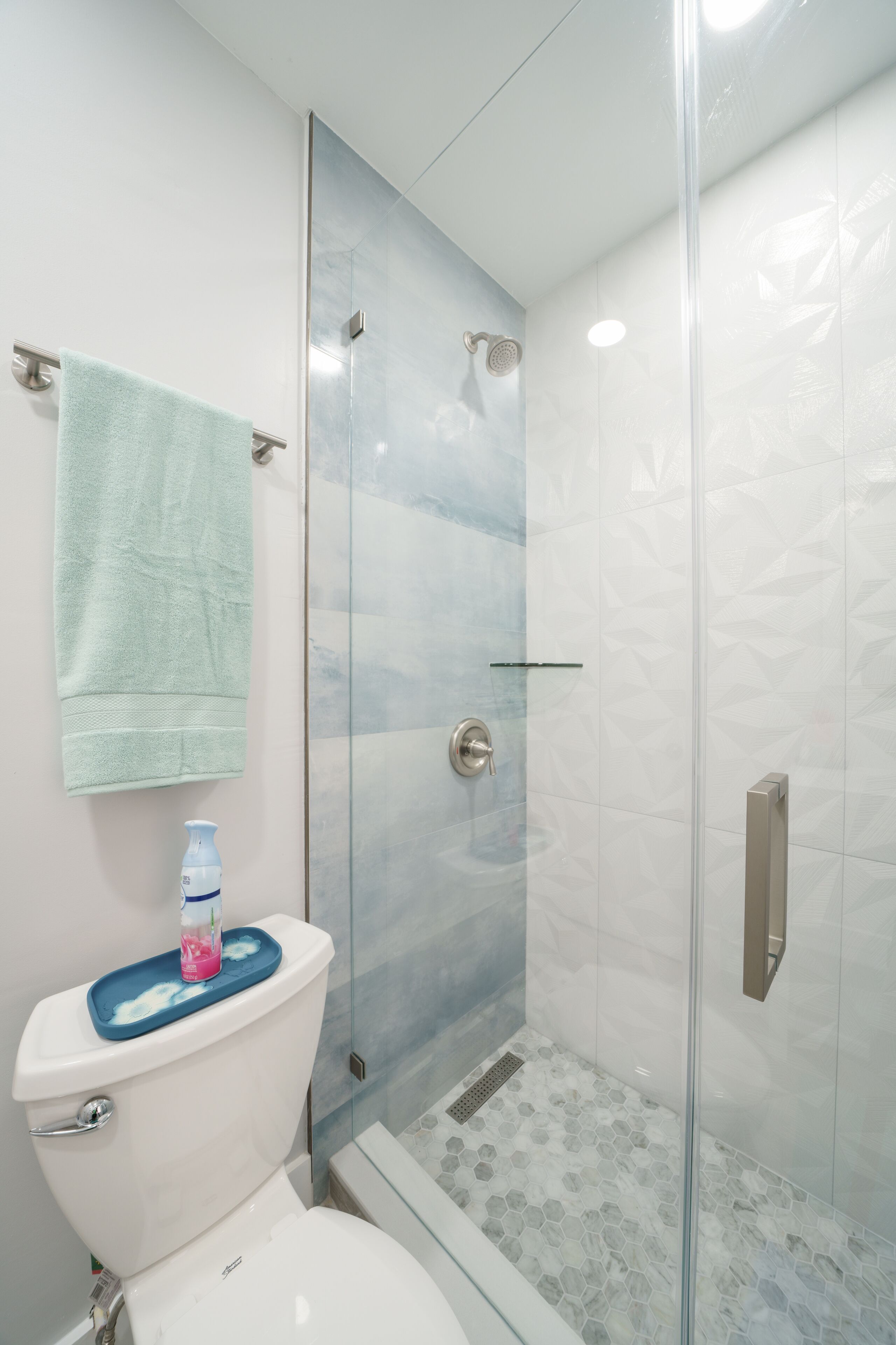 Un baño con ducha de vidrio, inodoro con felpudo azul y toalla colgada en la pared.
