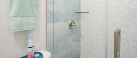 Un baño con ducha de vidrio, inodoro con felpudo azul y toalla colgada en la pared.