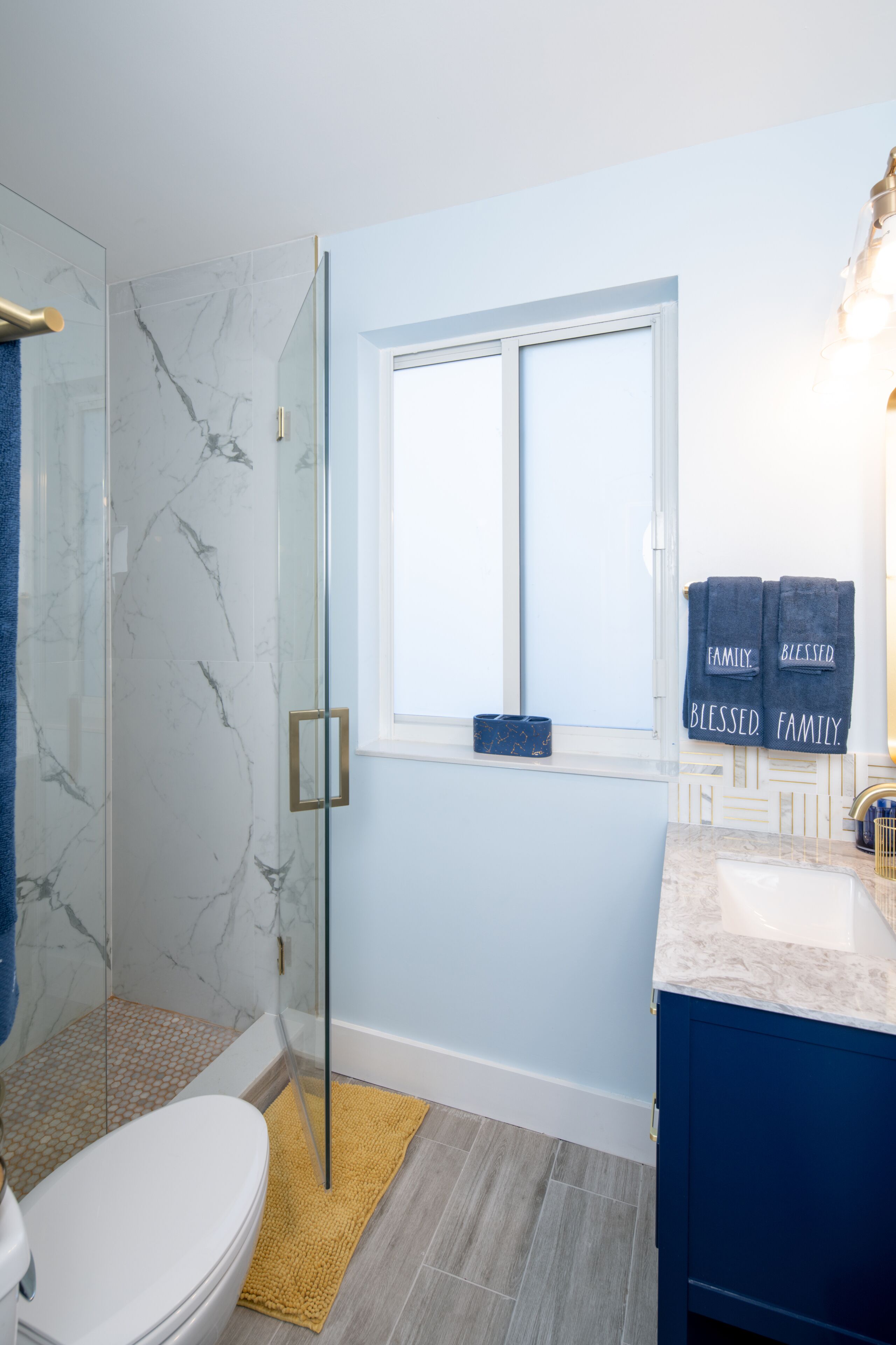 Ein Badezimmer mit einer Duschkabine aus Glas, einer weißen Toilette, einem blauen Waschtisch und zwei Handtüchern, die an der Wand hängen.