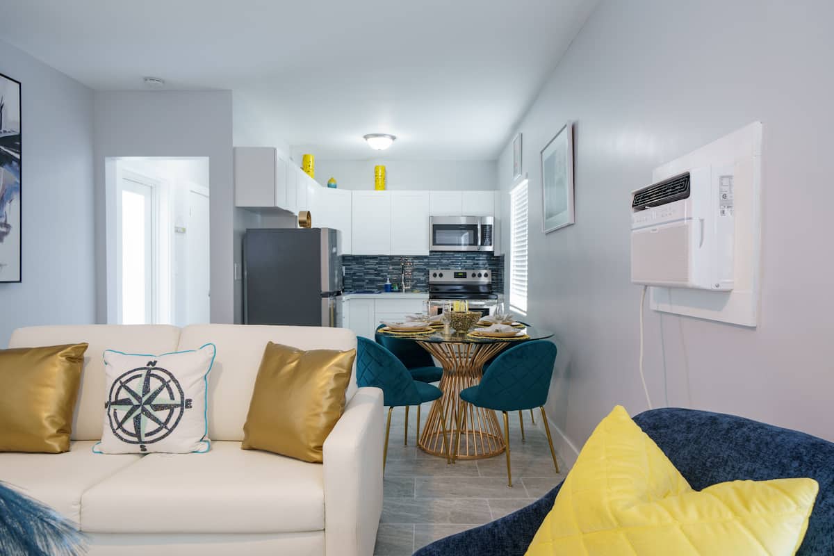 A modern living room with a sofa, a dining table with chairs, and a kitchen in the background.