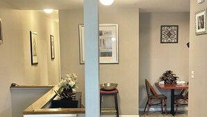 Een eethoek met een houten tafel en stoelen, een klein krukje met een kom, en ingelijste foto's aan de muur.