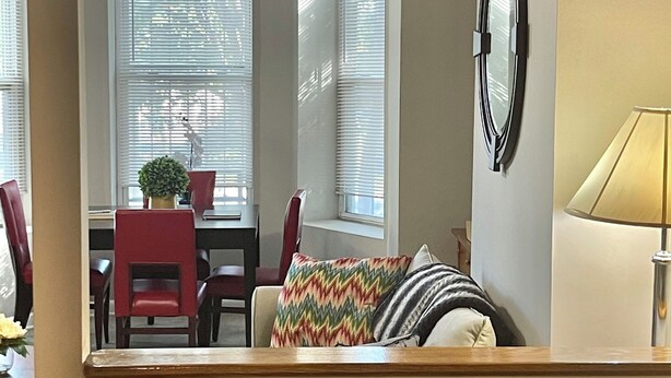 Een eethoek met een tafel, stoelen en een raam met jaloezieën.