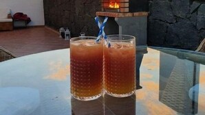 Uma mesa de vidro com duas bebidas e um forno de tijolos ao fundo.