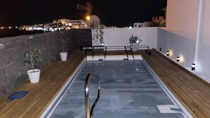 Terraço no telhado com piscina, plantas em vasos e vista da cidade à noite.