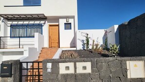 Uma casa moderna de dois andares com porta de madeira, parede de pedra e um pequeno jardim com plantas.