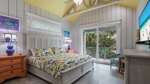 Ein Schlafzimmer mit einem Bett, Nachttischen aus Holz, einem Deckenventilator, einem Fenster mit Jalousien und einem Balkon mit einem Stuhl.