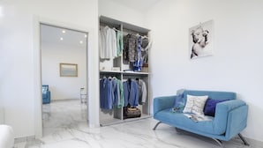 Una habitación moderna con un sofá azul, un vestidor con ropa colgada y suelo de mármol.