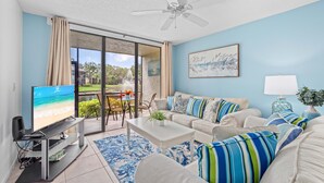 A living room with a television, sofa, coffee table, and a view of a beach through a sliding glass door. - *Casa Bella* Waterfront View! 2BR, w/2 Pools, Mins to IMG/Beach/Anna Maria Isl (Bradenton)