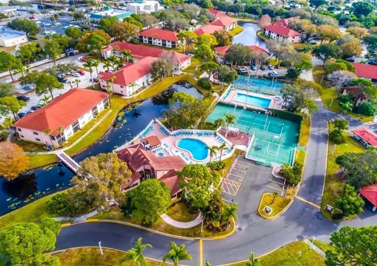 An aerial view of a residential area with a swimming pool, tennis court, and a curved road.