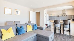 A modern apartment with a grey sectional sofa, a kitchen with grey tiles, and a dining area with bar stools. - Luxury apartments with sea and pier views, right in the heart of North Norfolk. (Cromer)