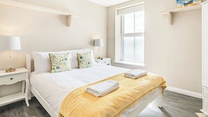 A neatly arranged bedroom with a large bed, bedside tables, a window, and a painting on the wall. - Luxury apartments with sea and pier views, right in the heart of North Norfolk. (Cromer)