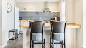 A modern kitchen with a central island, two bar stools, a built-in oven, and a stainless steel sink. - Luxury apartments with sea and pier views, right in the heart of North Norfolk. (Cromer)