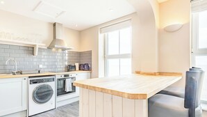A modern kitchen with a built-in oven, microwave, and washing machine, a wooden island, and a large window providing natural light. - Luxury apartments with sea and pier views, right in the heart of North Norfolk. (Cromer)
