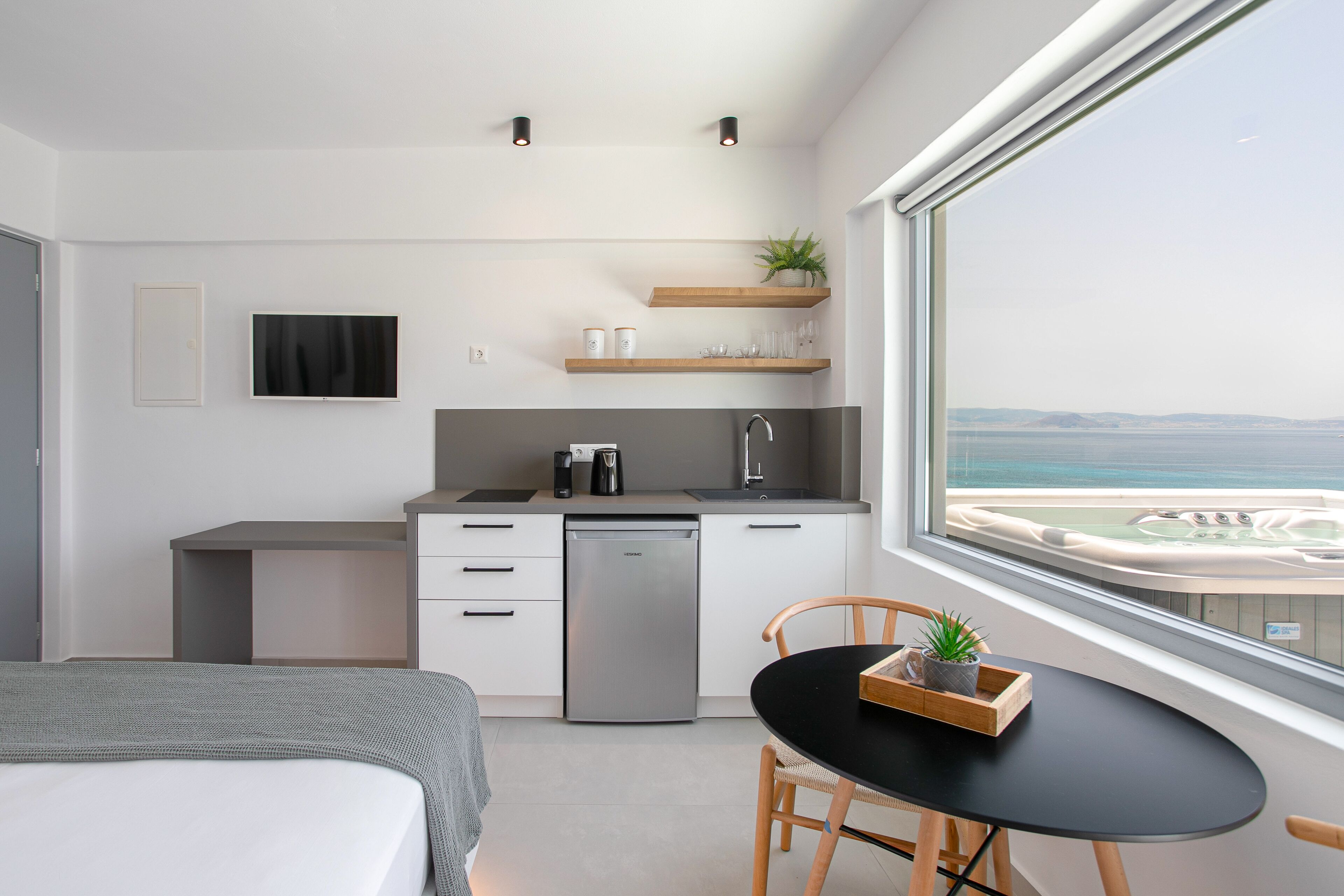 Una cocina moderna con lavavajillas, cafetera y fregadero. Hay una mesa de comedor con una silla y una planta pequeña encima. Un ventanal ofrece vistas al mar.