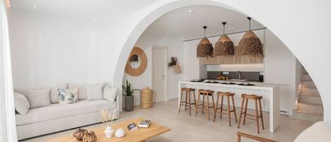 Ein modernes Wohnzimmer mit einer Couch, einem Holztisch und einer Küchenzeile mit Bar und Hockern.