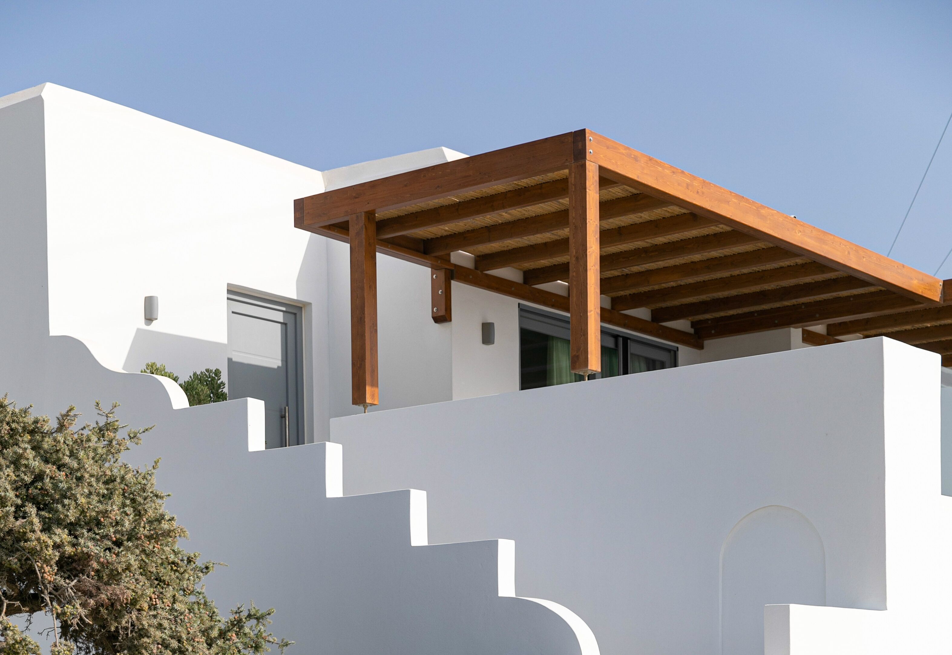 A modern building with a white facade, wooden pergola, and a clear sky.