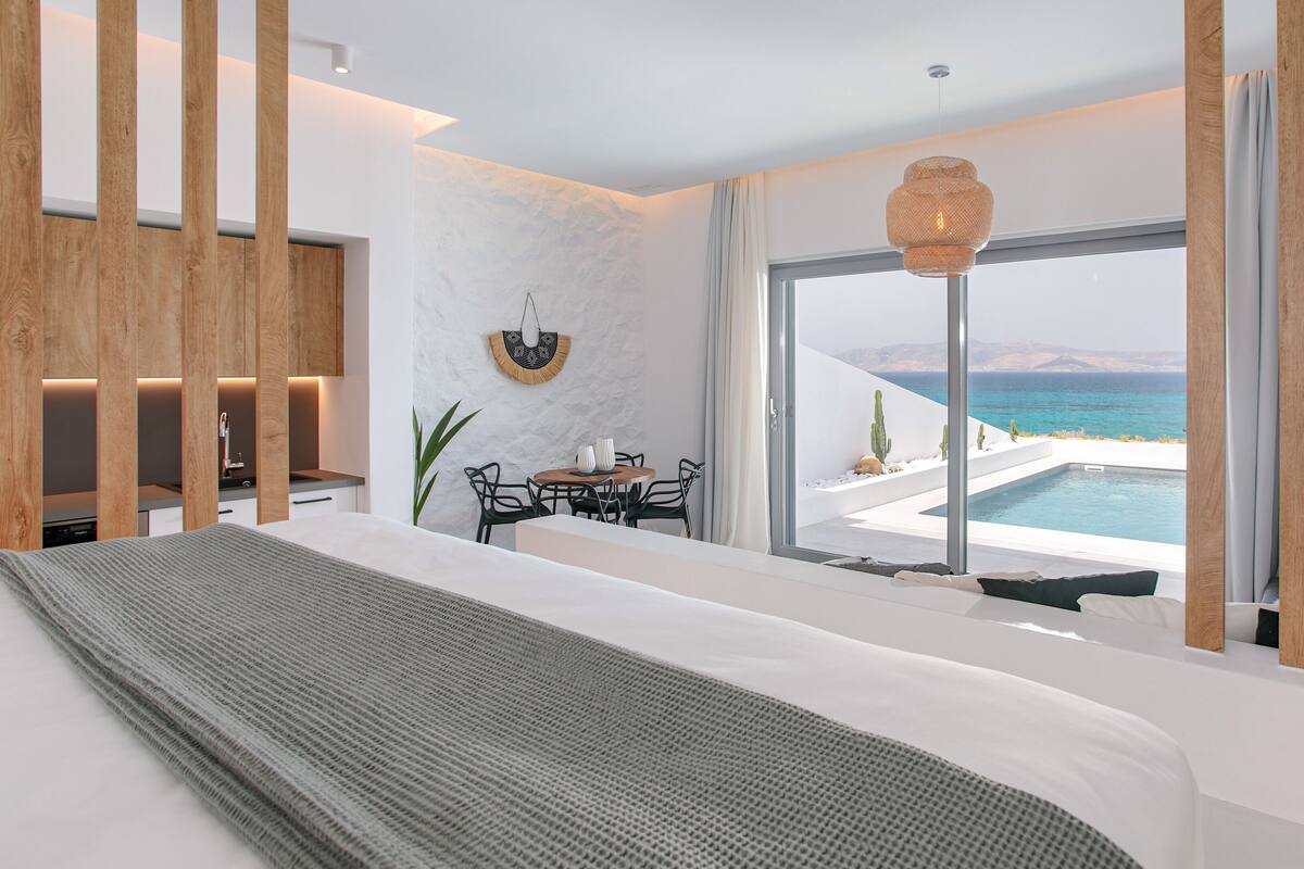 Una habitación de hotel moderna con una cama grande, un comedor y vistas al mar.