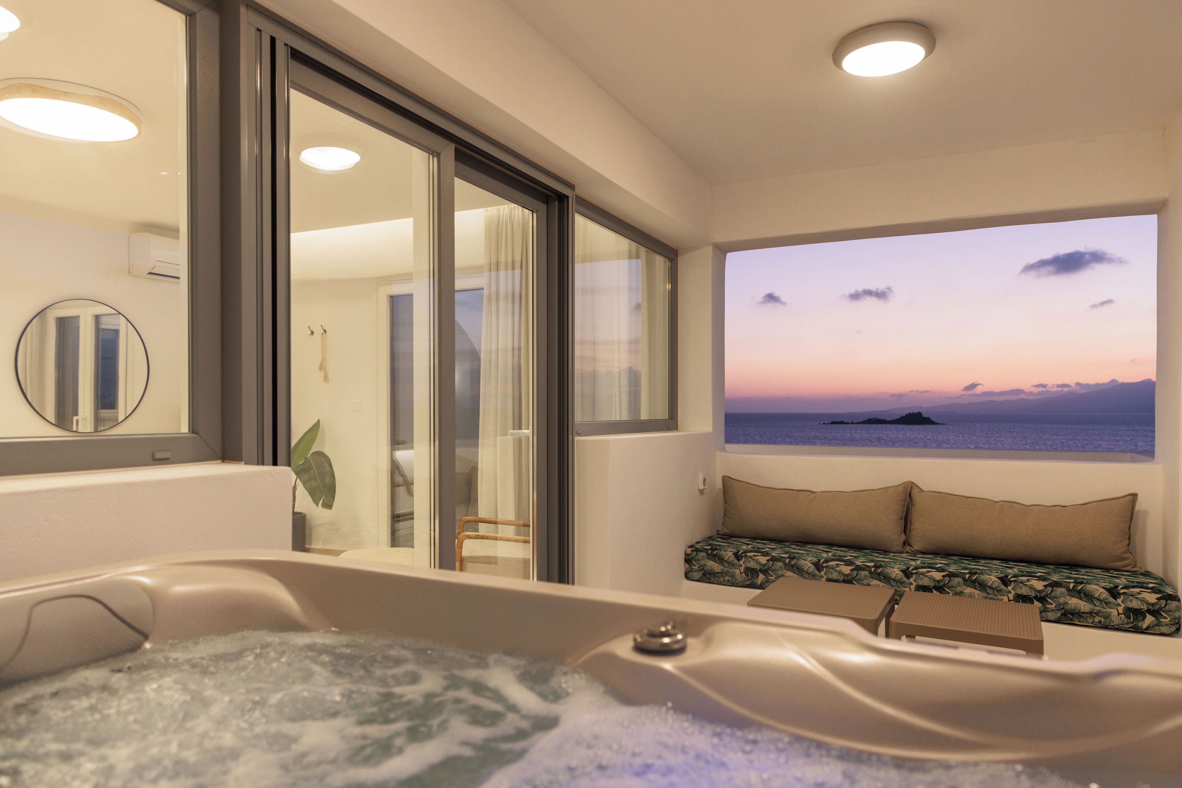 Une salle de bain moderne avec une baignoire, un grand miroir et une vue sur la mer au coucher du soleil.