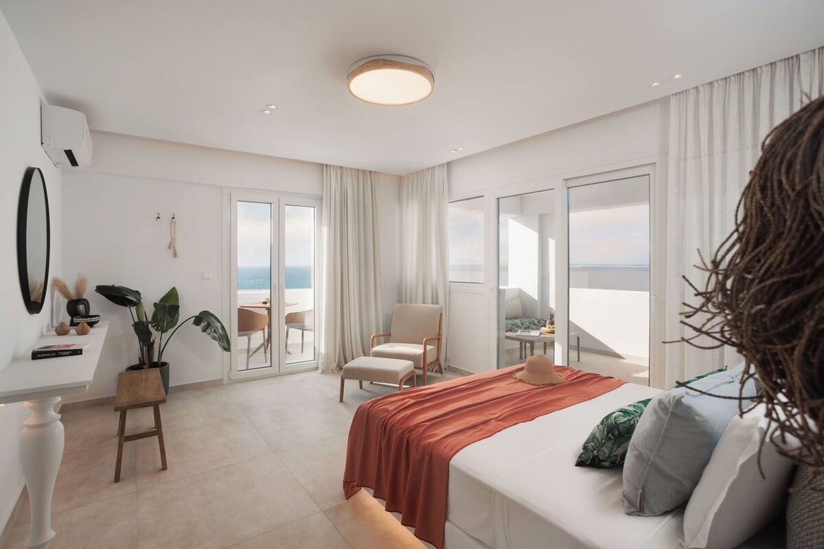 Una habitación de hotel moderna con una cama grande, una zona de estar con vistas y un balcón.