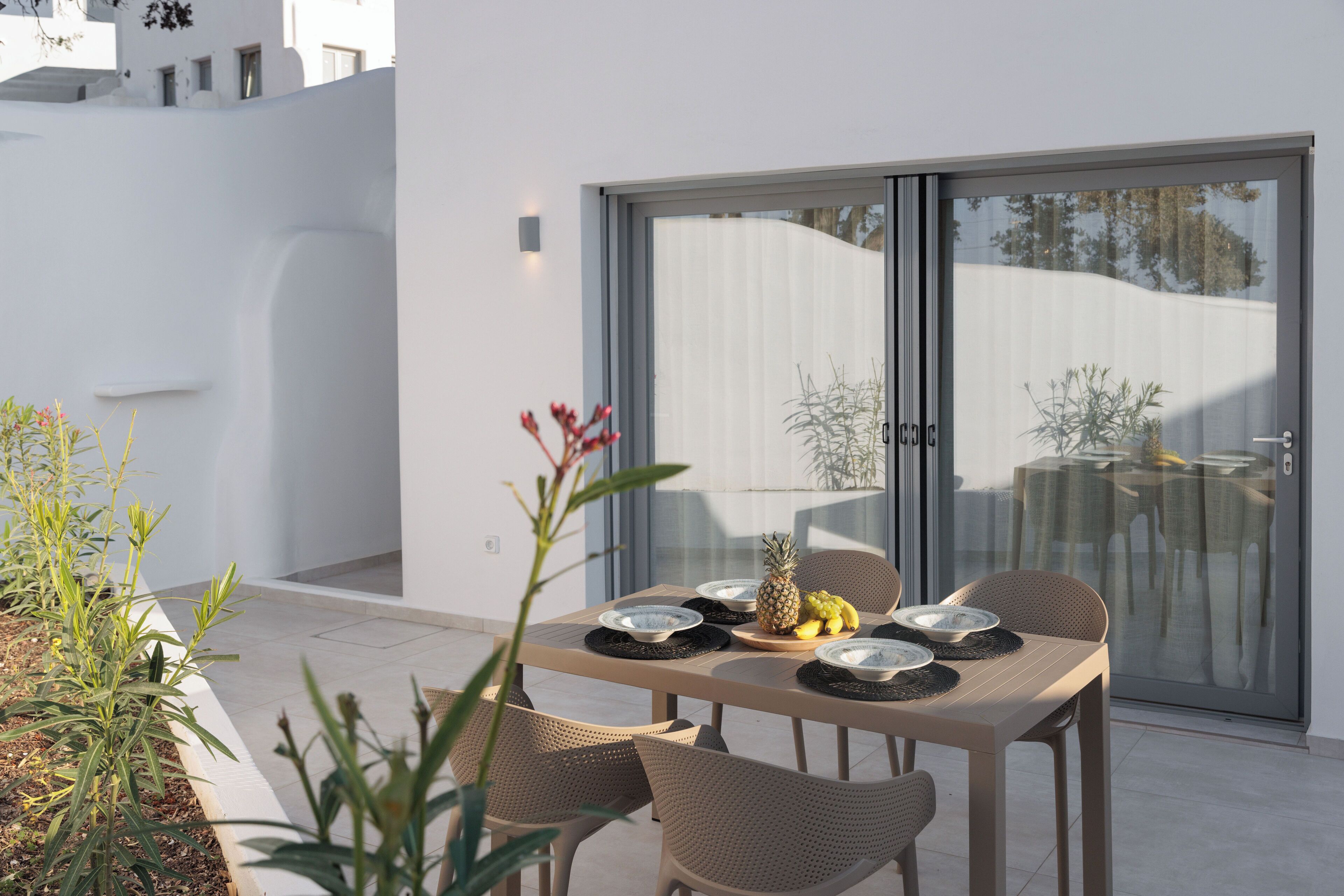 An outdoor dining area with a table set for four, surrounded by wicker chairs, and a sliding glass door leading to a patio.