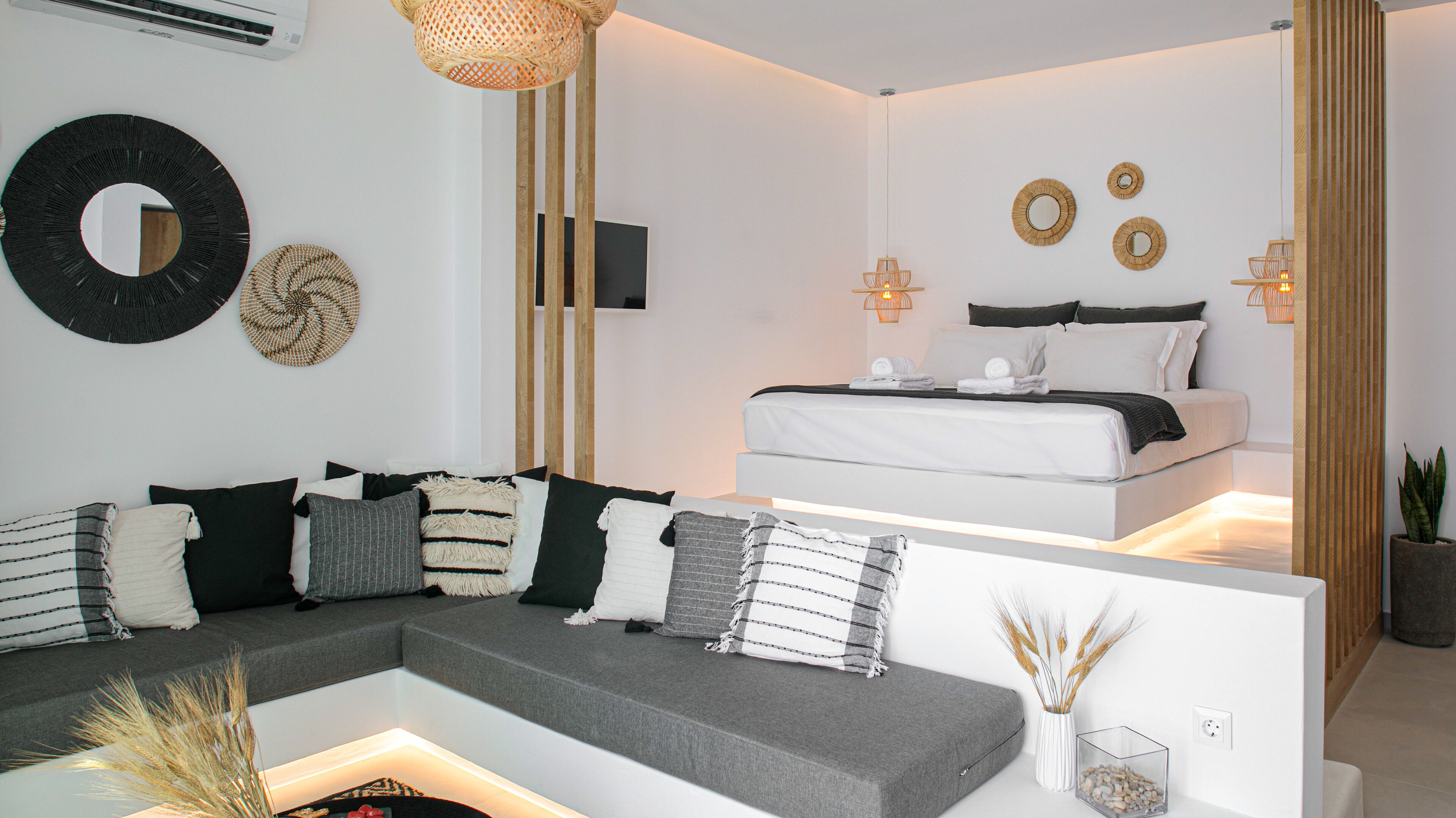 Une chambre moderne avec un canapé gris, un lit avec une literie blanche et des œuvres d’art décoratives au mur.
