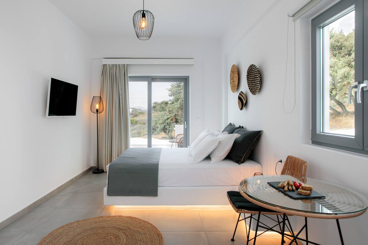 Un dormitorio moderno con cama, televisión, mesa de comedor y vistas al exterior.