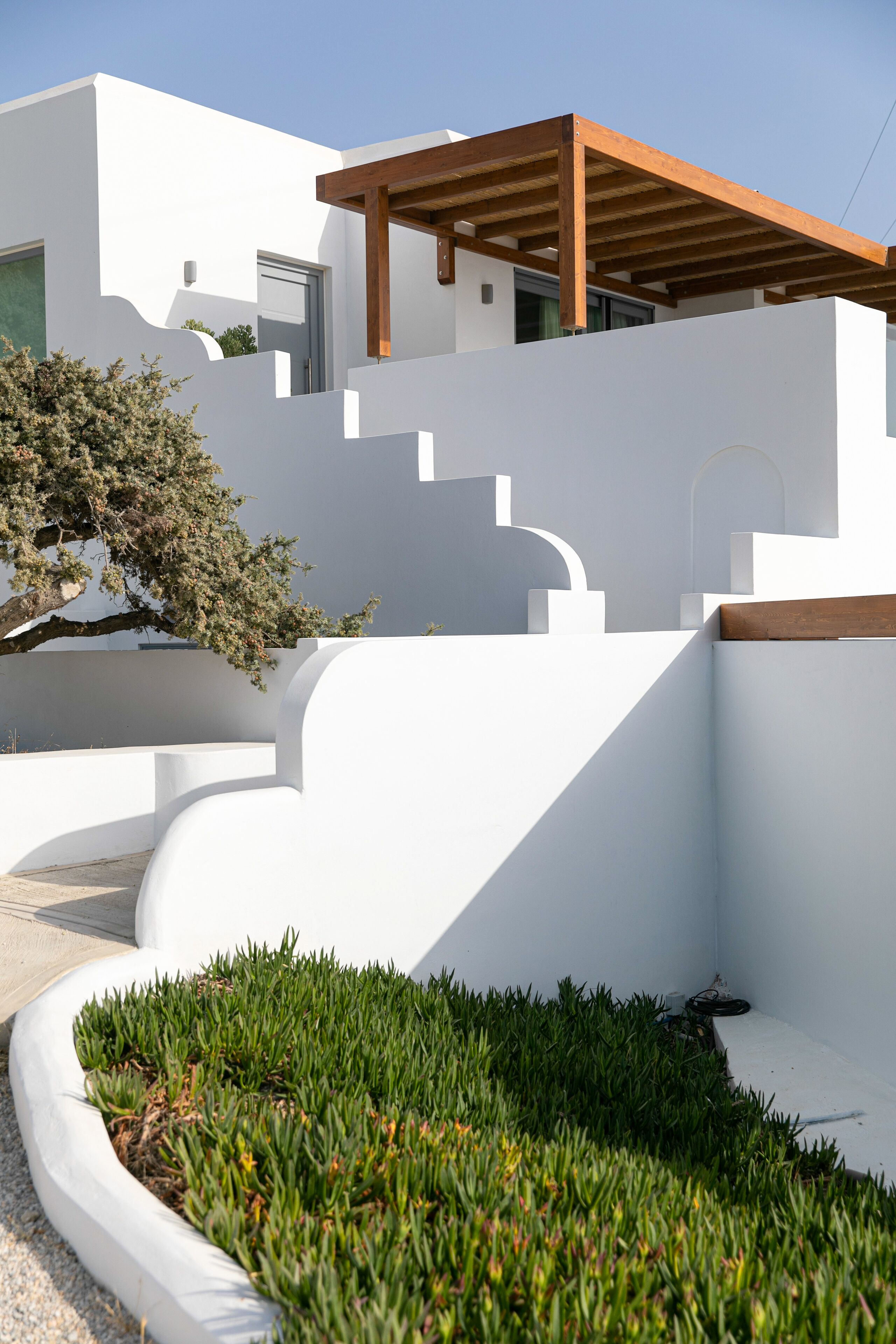 A modern white building with a wooden pergola and a landscaped garden area.