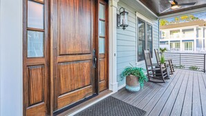 A wooden front door with a glass panel, a porch with a bench and potted plants, and a view of a building in the background. - 3 Shore Crest, Chefs Kitchen, Free Golf, Game Room, Beach, Pool (Hilton Head)