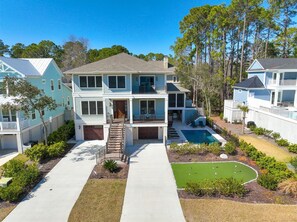 A two-story house with a front porch, a swimming pool, and a small golf course.