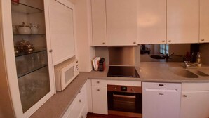 A compact kitchen with white cabinets, a microwave, an oven, a dishwasher, and a sink. - Italian designed apartment Marais (Paris)
