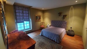 A bedroom with a large bed, a wooden nightstand, a chair, a window with curtains, and a small table with a lamp. - Italian designed apartment Marais (Paris)
