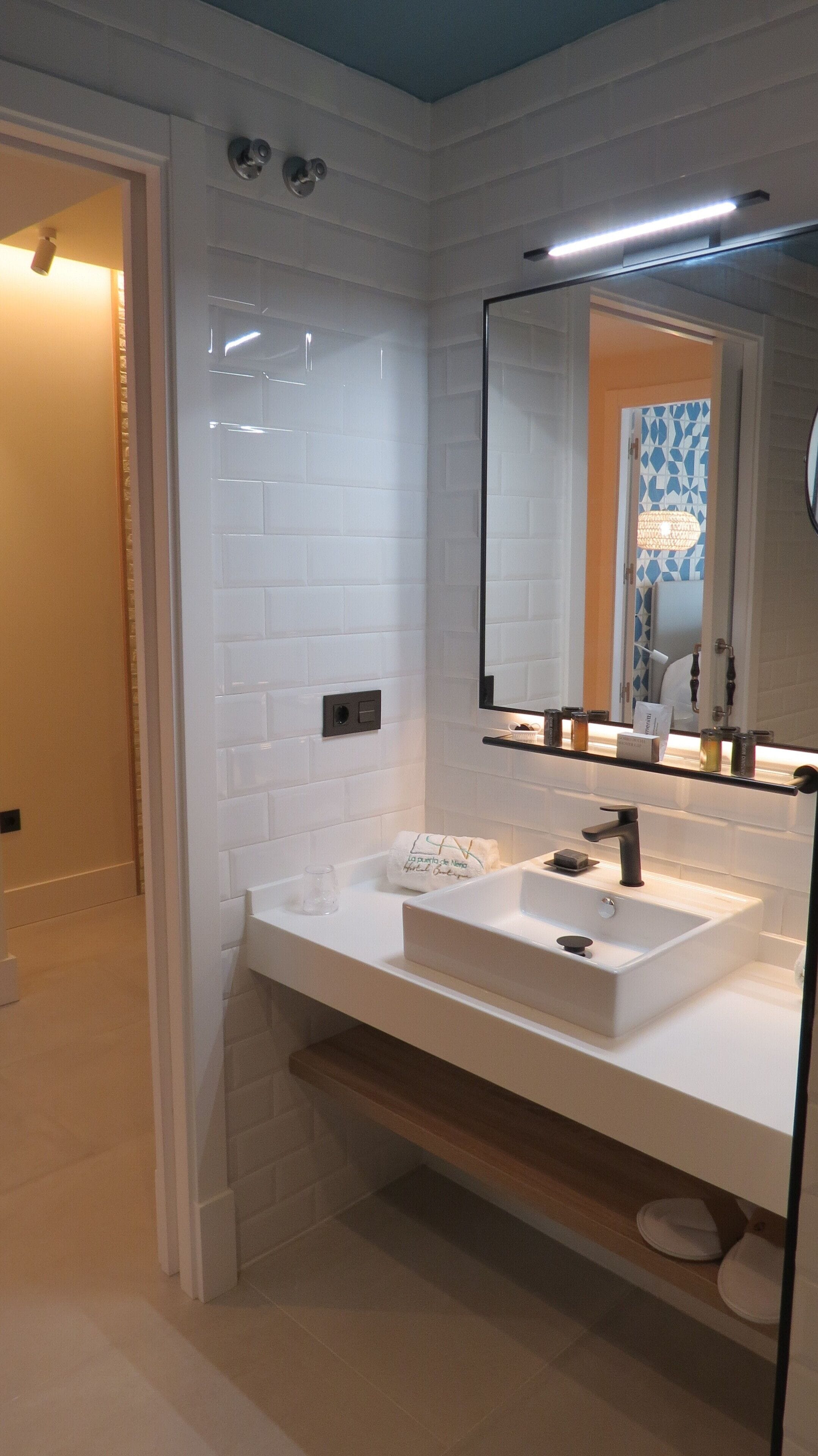 Un baño moderno con azulejos blancos tipo metro, un espejo grande, un lavabo blanco y un perchero para toallas.