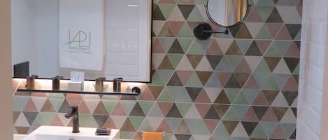 A bathroom with a geometric patterned wall, a mirror, a sink, and a towel rack.