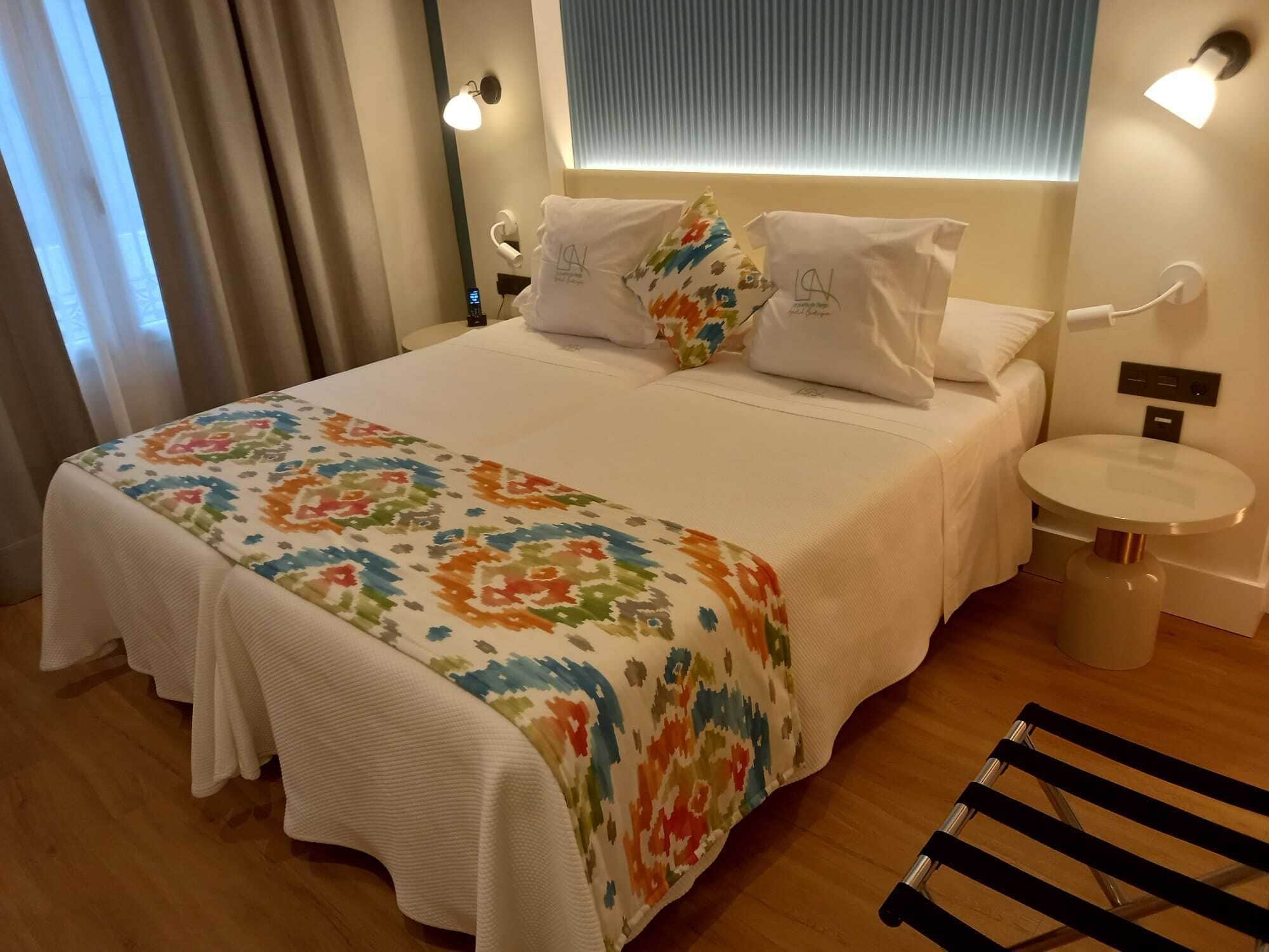 Een hotelkamer met een bed, nachtkastje, stoel en een klein rond tafeltje.