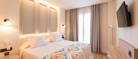A hotel room with a large bed, two bedside tables, a desk, a television, and a window with curtains.
