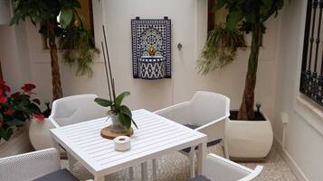 A small outdoor patio with a white table and chairs, surrounded by potted plants and a decorative tile wall.