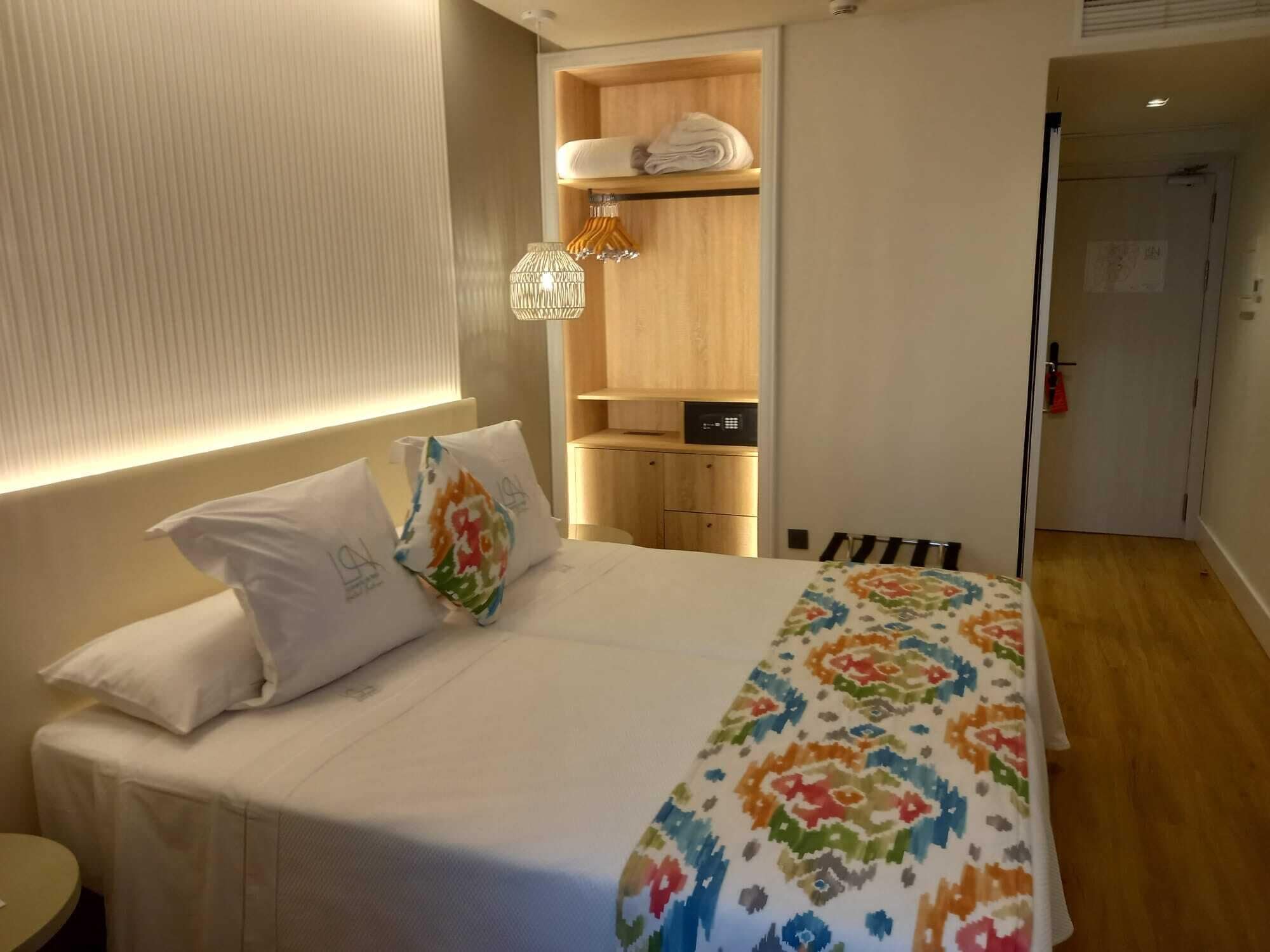 A hotel room with a bed, a bedside table, a wardrobe, and a small bathroom area.