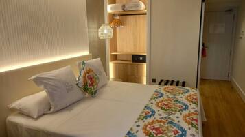 Una habitación de hotel con cama, mesita de noche, armario y un pequeño baño.
