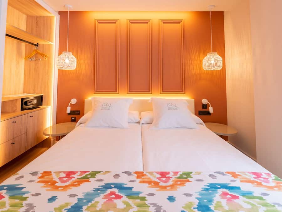 A hotel room with a bed, two bedside tables, a wardrobe, and a hanging light fixture.