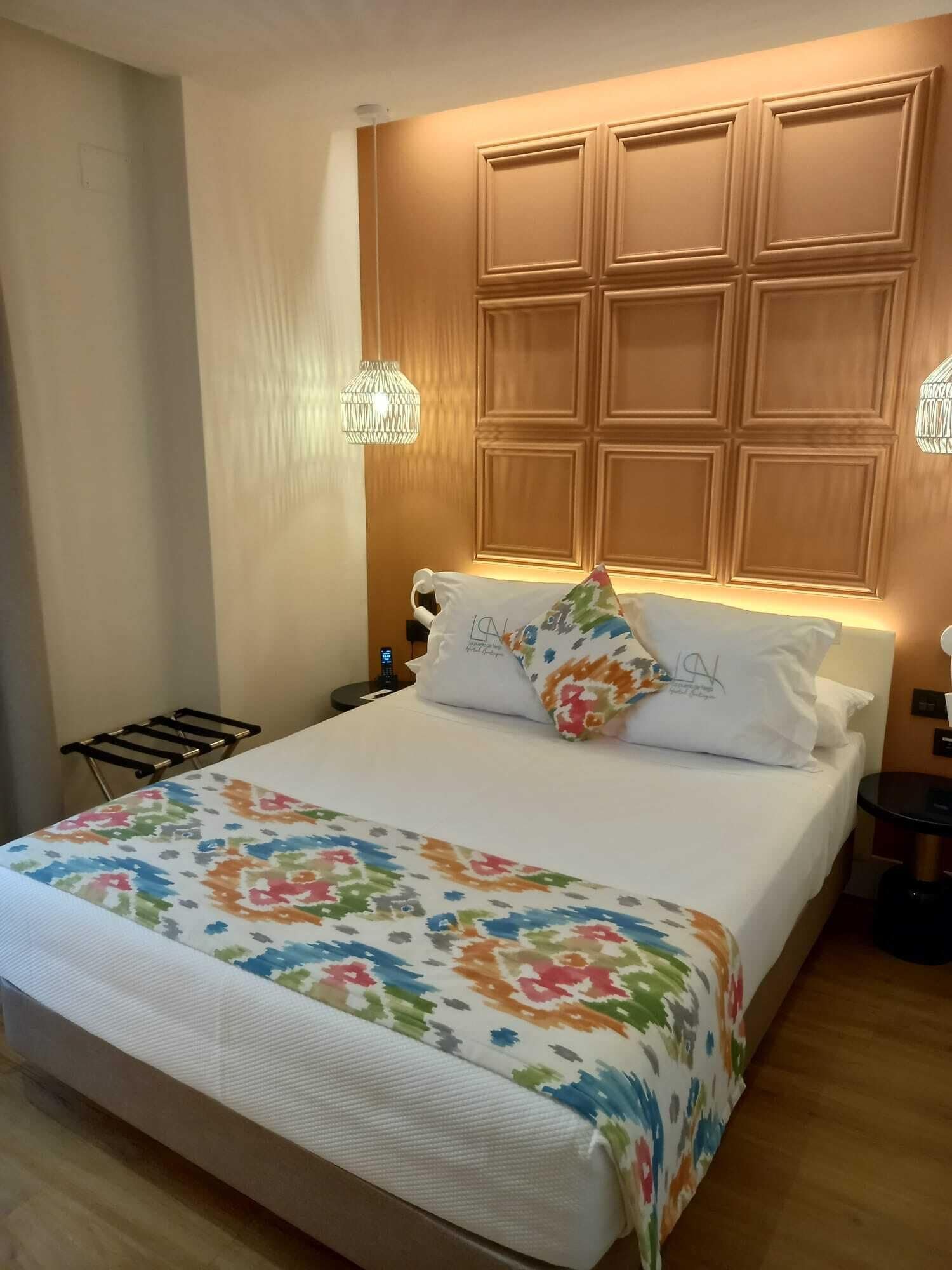 Een hotelkamer met een groot bed, een houten hoofdbord, twee nachtkastjes en een bijzettafeltje.