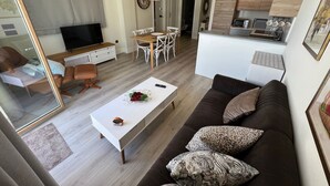 Una sala de estar moderna con un sofá, una mesa de centro y un televisor. Se observa un comedor con sillas y una mesa. Se distingue una cocina al fondo.