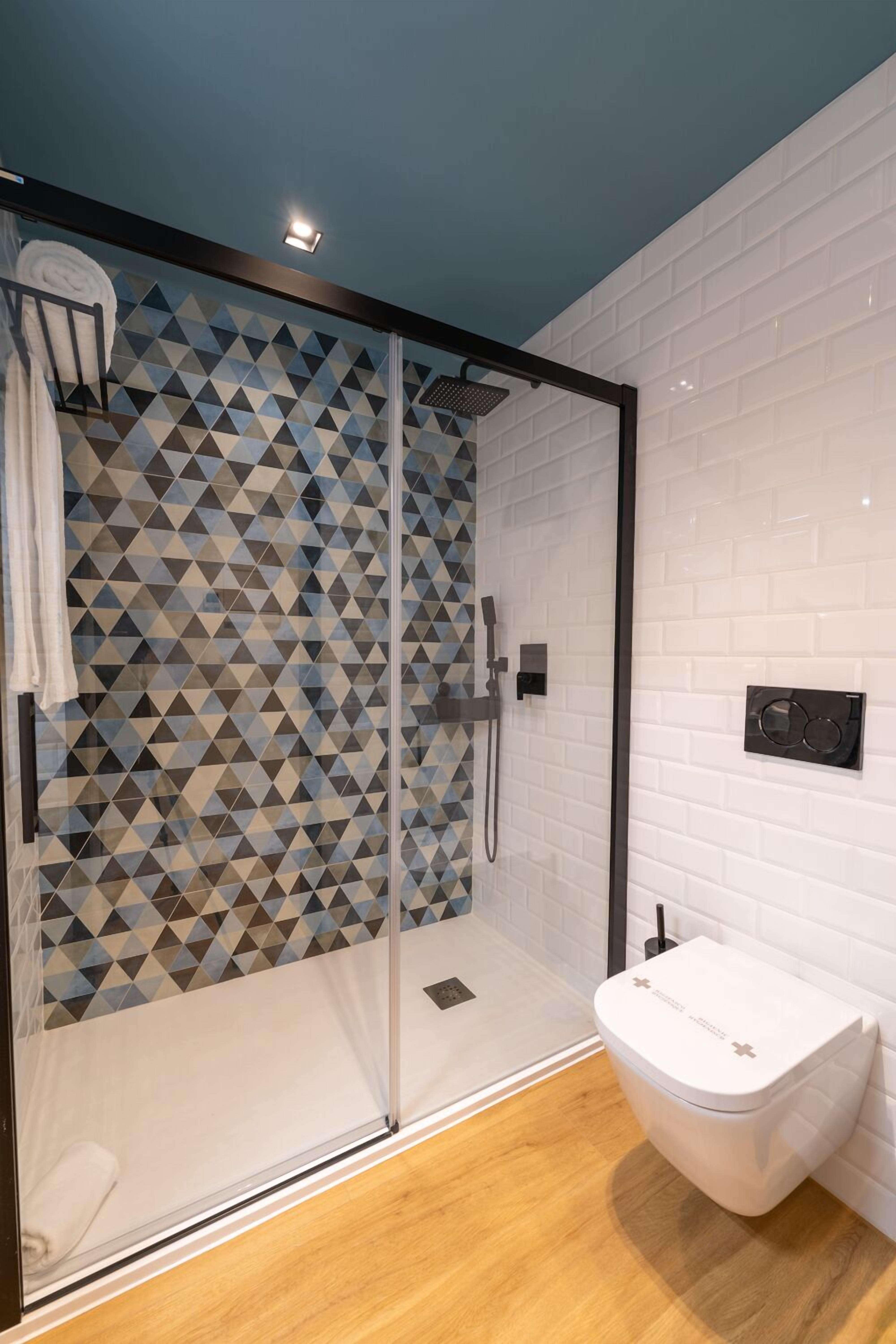 A modern bathroom with a glass-enclosed shower, white tiled walls, and a wooden floor.