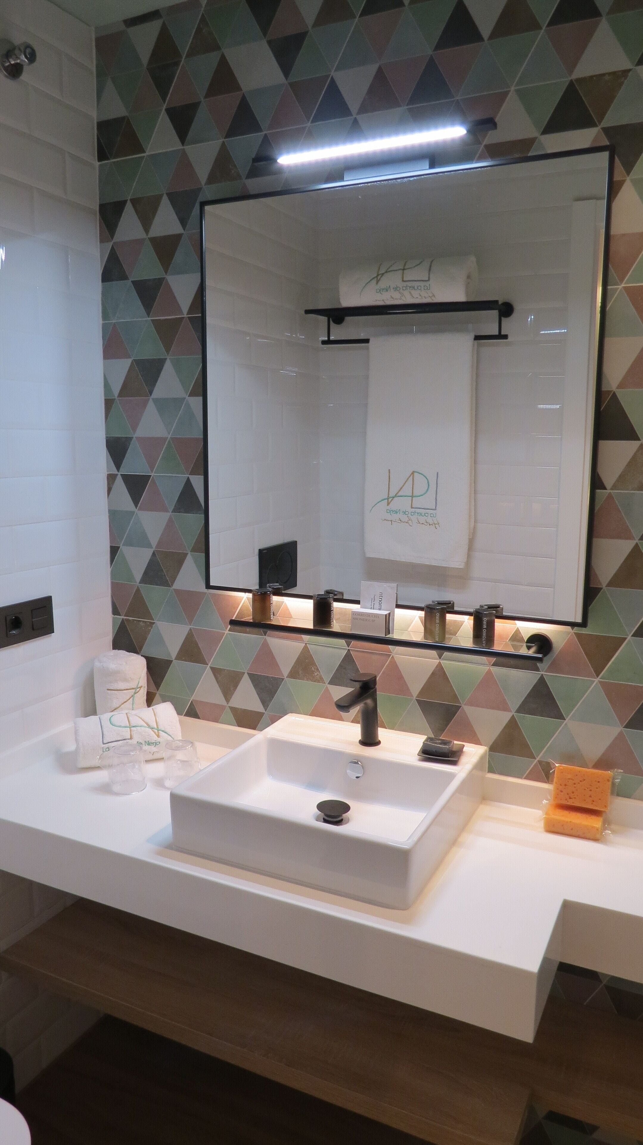 Un baño con un lavamanos blanco, un espejo y una pared con estampado geométrico.