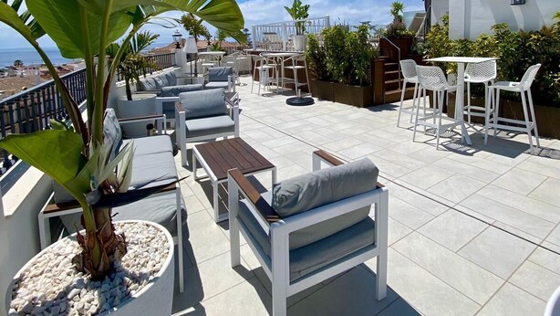 Una terraza en la azotea con mobiliario exterior, plantas en macetas y vistas despejadas al océano.