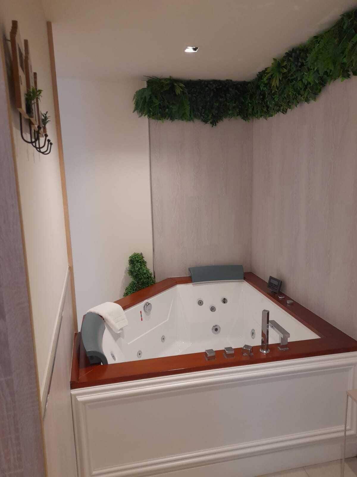 Un baño moderno con una bañera independiente, una pequeña planta en maceta y un aplique de pared.