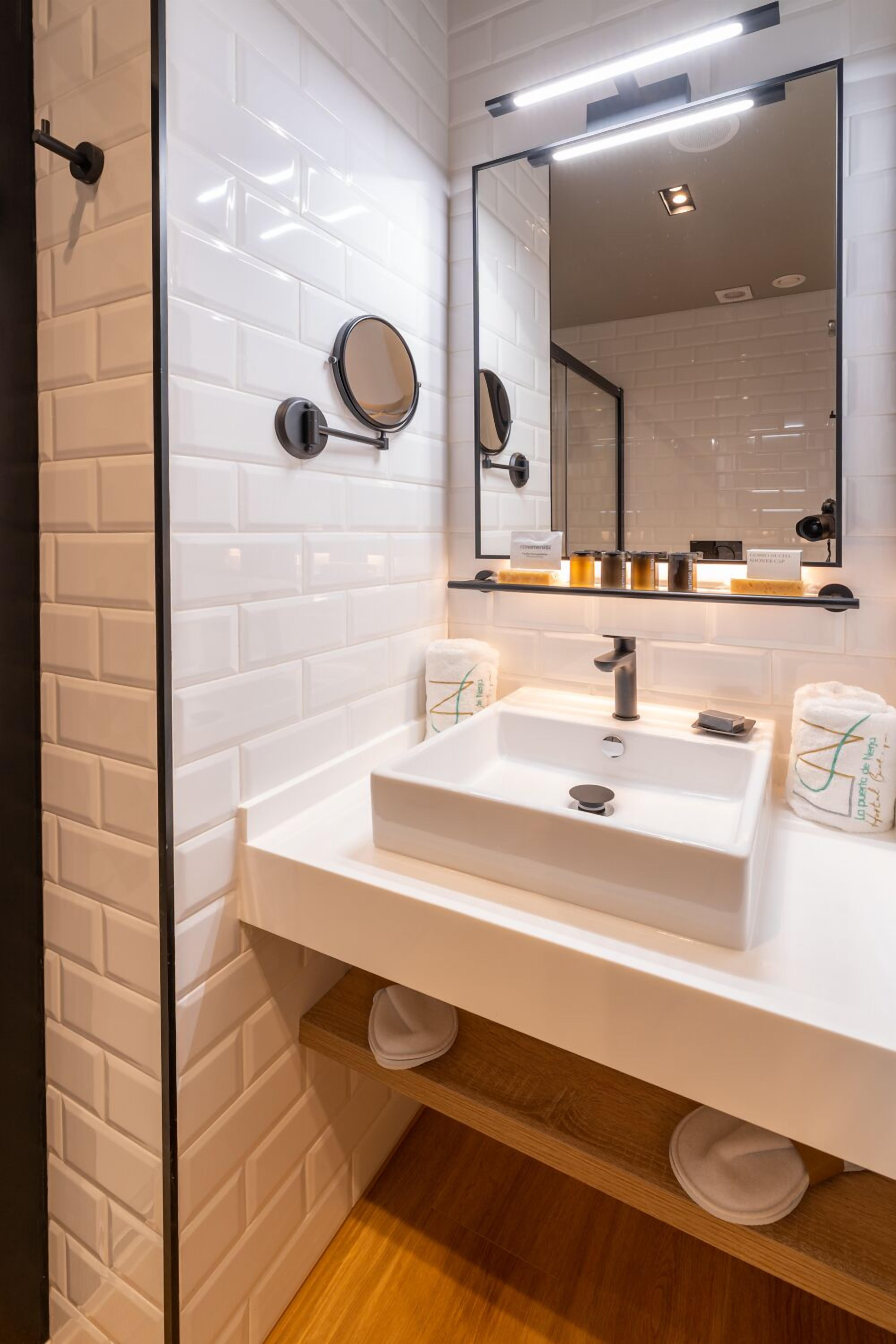 A modern bathroom with white subway tiles, a white sink, a mirror, and a shelf with toiletries.