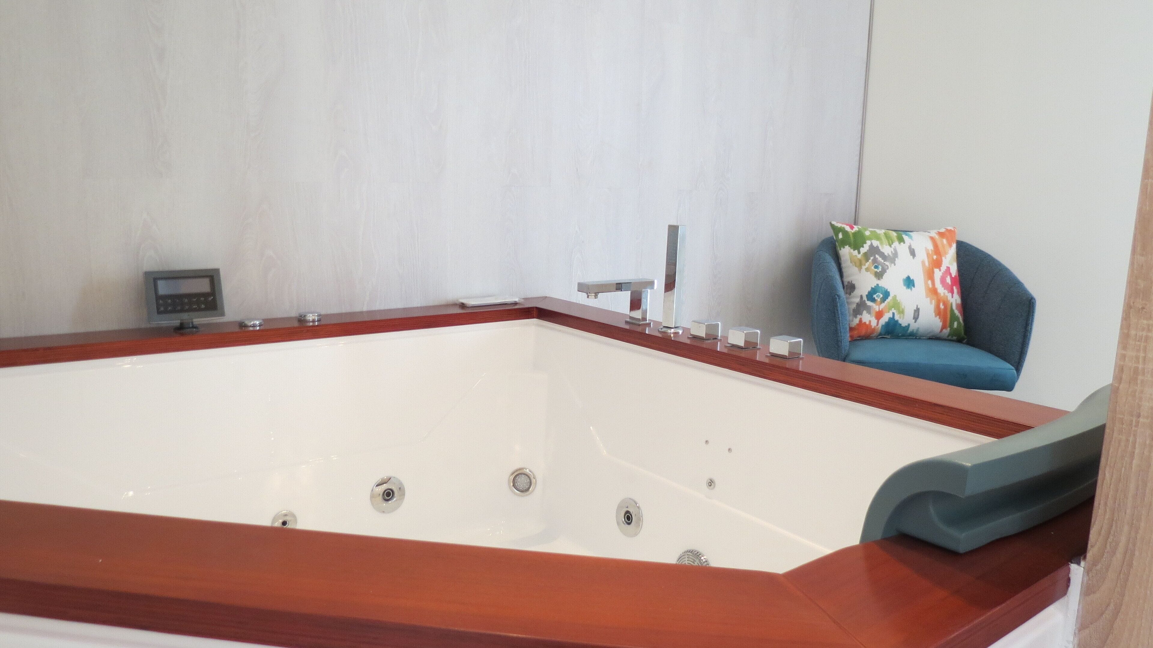 A modern bathroom with a freestanding bathtub, a small control panel, and a blue chair with a colorful pillow.