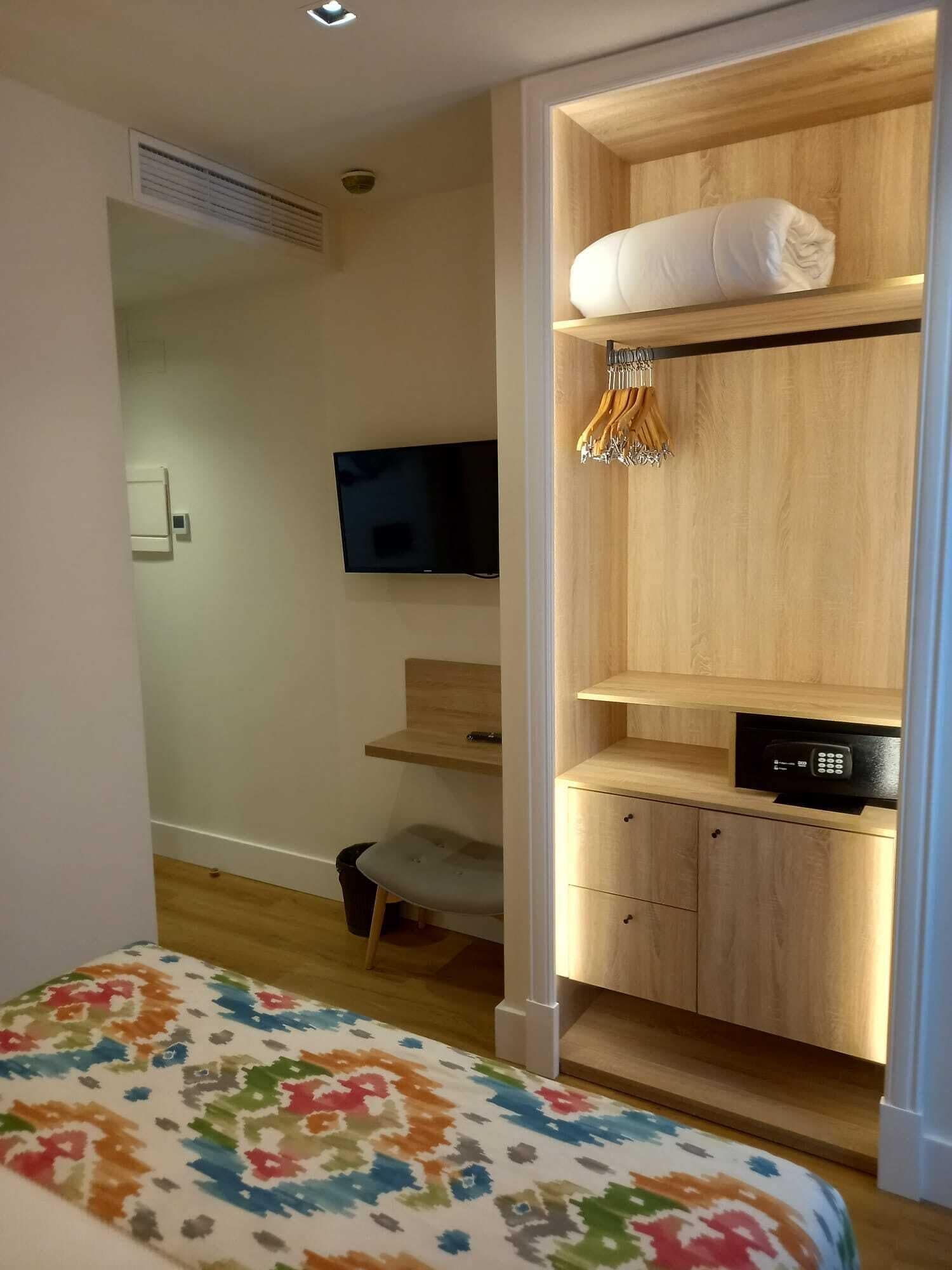 Een slaapkamer met een bed, een televisie, een houten kledingkast en een kleine stoel.